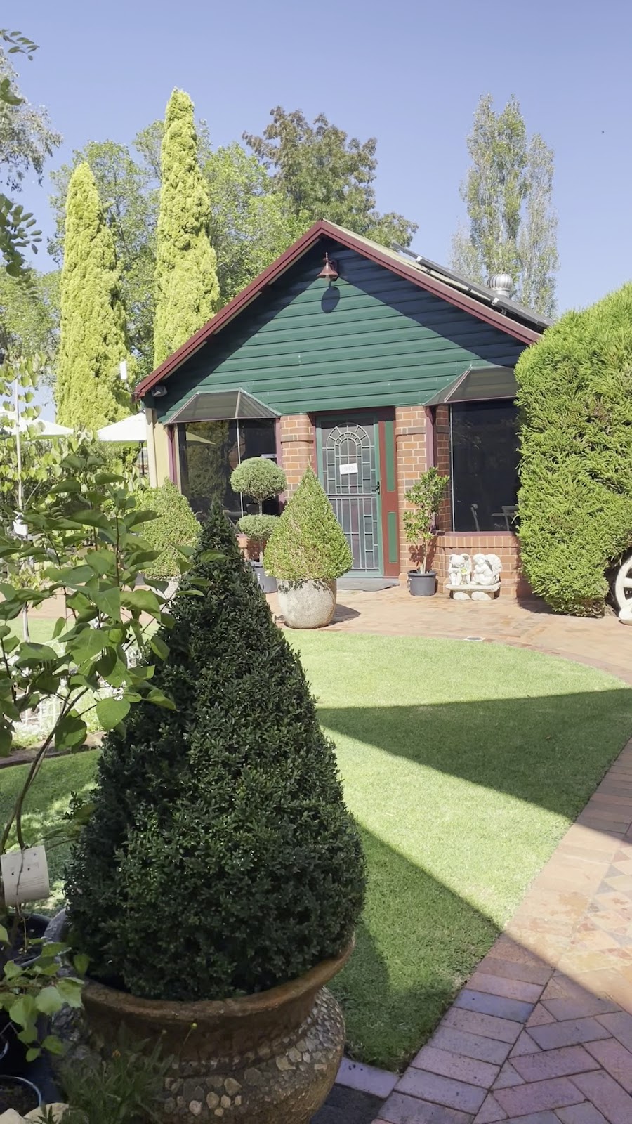 A green garden cottage with a clipped topiary cone on the lawn